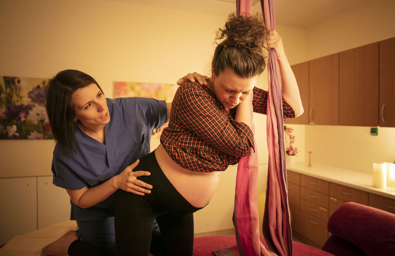 Healthcare Fotografie: Im Kreissaal bereitet sich eine werdende Mutter auf die Geburt vor. Sie trägt noch ihre Kleidung. Eine Hebamme unterstützt sie.