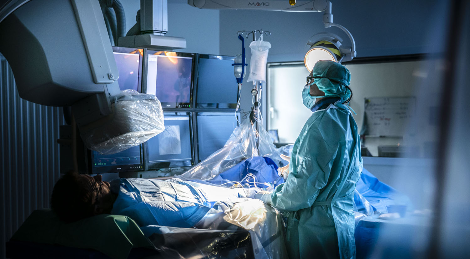 Healthcare Fotografie: Ein Kardiologe führt eine Herzkatheter-Untersuchung durch. Der Raum ist abgedunkelt, der Arzt in OP-Kleidung.
