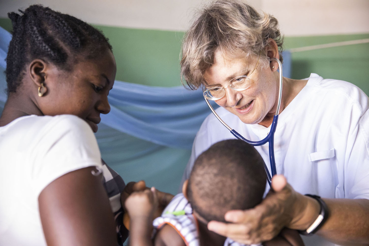 Healthcare Fotografie: Dr Elke Kleuren-Schrievers untersucht in der Kinderstation eines afrikanischen Krankenhauses ein Säugling. Die junge Mutter hält das Kind.